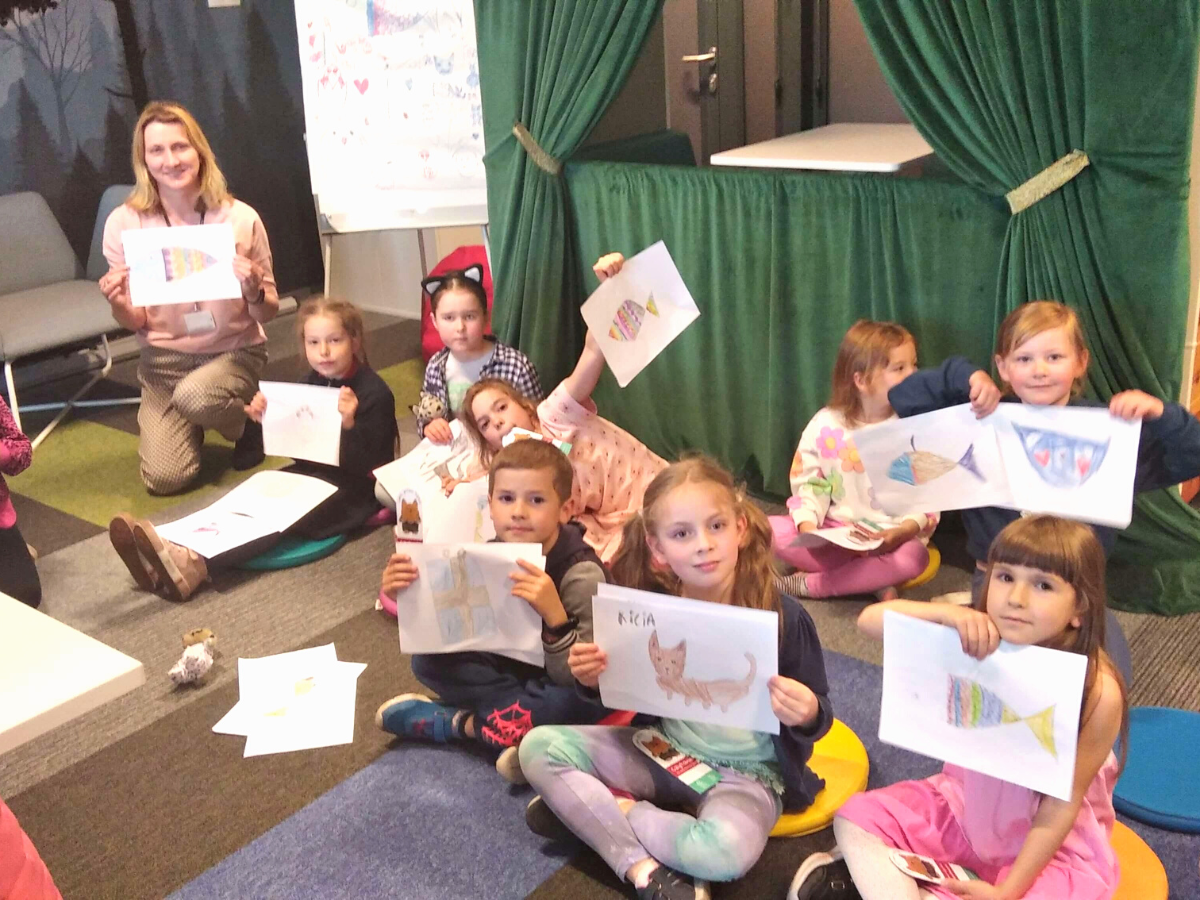 Pani bibliotekarka razem z dziećmi prezentuje wykonane na zajęciach rysunki