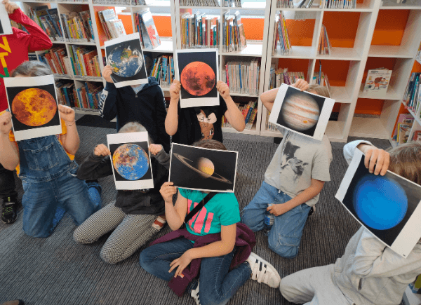 Dzieci pozują do zdjęcia, zasłaniając twarze zdjęciami planet