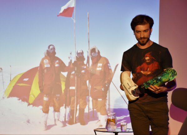 Na zdjęciu widoczny jest Jasiek Mela na scenie za nim widoczna jest prezentacja ze zdjęciami