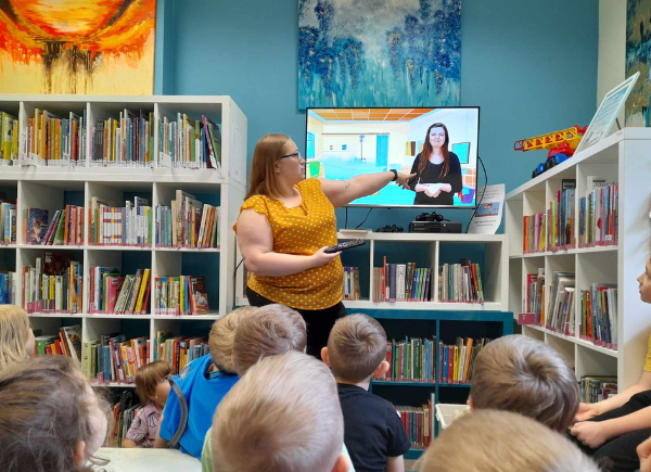 Zajęcia z przedszkolakami, bibliotekarka pokazuje na telewizor