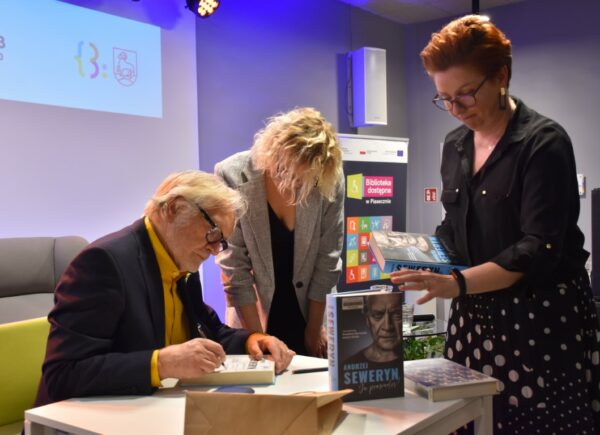 Andrzej Seweryn składający podpisy na książkach podczas spotkania autorskiego wraz z Sylwią Chojnacką-Tuzimek, Zastępcą Dyrektora Biblioteki, oraz prowadzącą spotkanie, Magdaleną Kwiatkowską