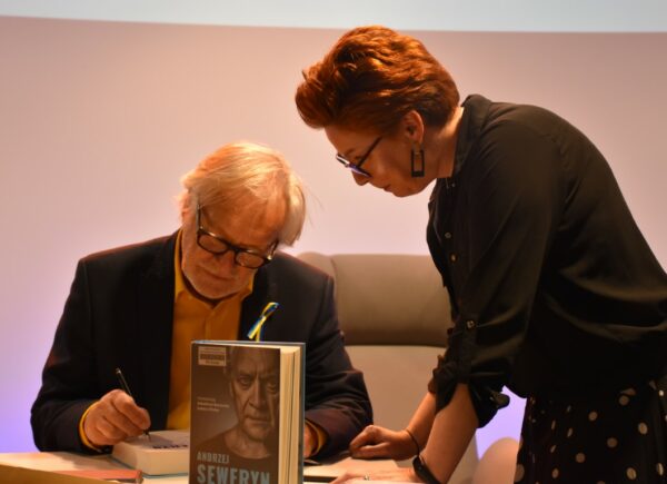 Andrzej Seweryn składający podpisy na książkach podczas spotkania autorskiego wraz z Sylwią Chojnacką-Tuzimek, Zastępcą Dyrektora Biblioteki
