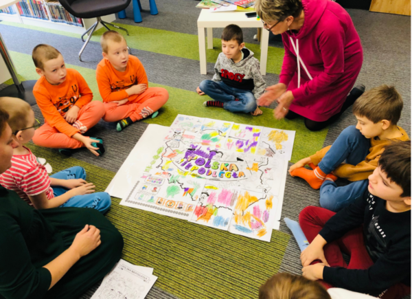 Dzieci siedzą na dywanie, przed nimi utworzona z pokolorowanych puzzli mapa Polski