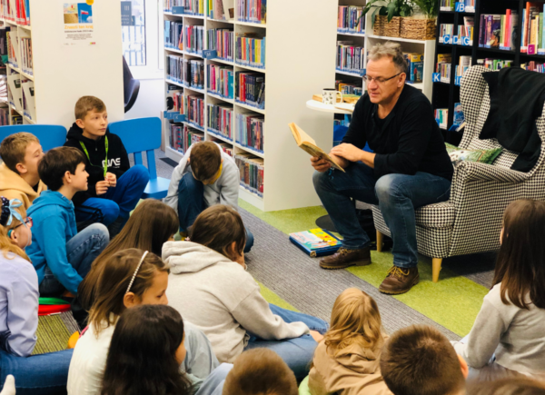 Autor Tomasz Trojanowski podczas spotkania autorskiego czyta dzieciom fragment jednej z ulubionych książek