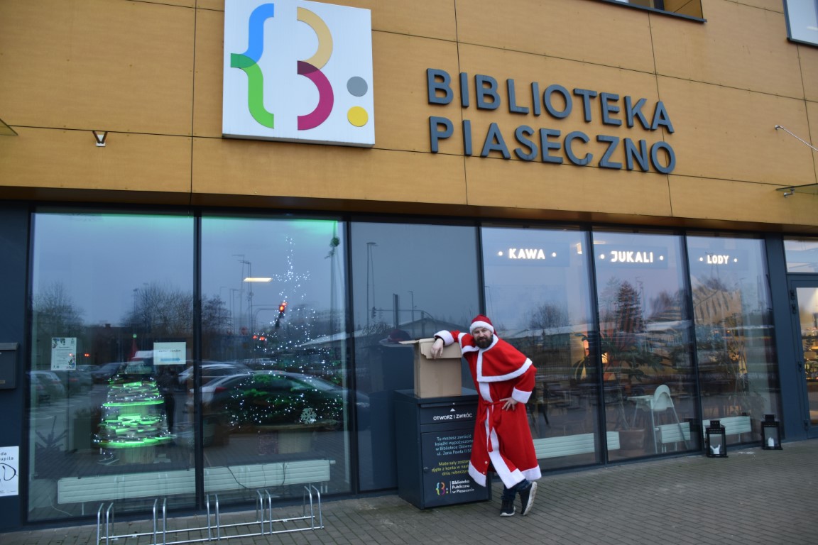 Jakub Ćwiek w stroju świętego mikołaja przed budynkiem Biblioteki Publicznej w Piasecznie
