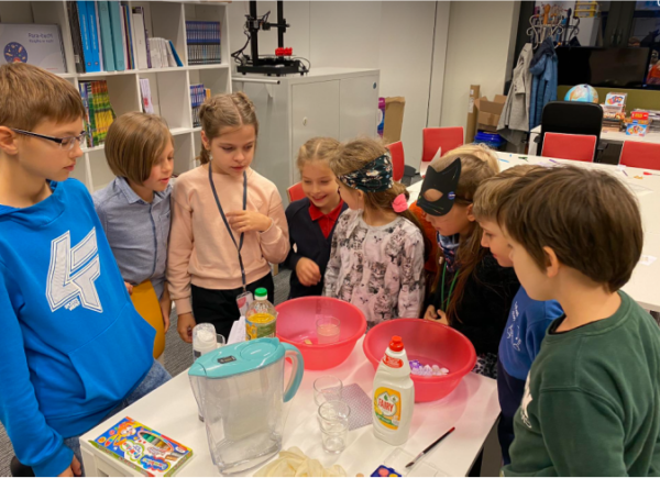 Na zdjęciu dzieci oglądają przygotowania do eksperymentu z wodą.