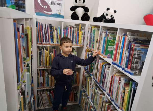 Chłopiec szuka papierowych bombek między książkami