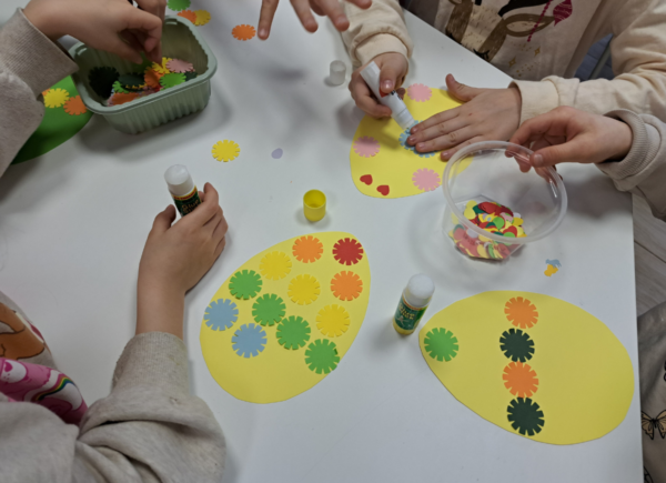 Dzieci naklejają kolorowe elementy na papierowe pisanki