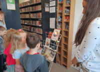 Pani bibliotekarka pokazuje przedszkolakom wystawkę z okazji Dnia bibliotekarza i bibliotek